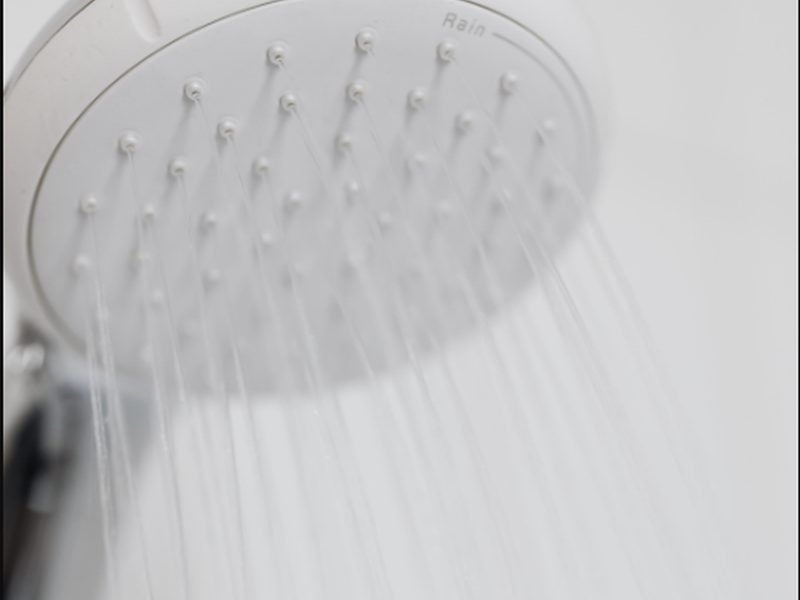 Detalhe de chuveiro tipo chuva branco com água caindo